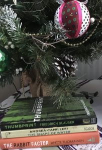 A stack of books underneath a Christmas tree, all are the first in a series of detective mysteries