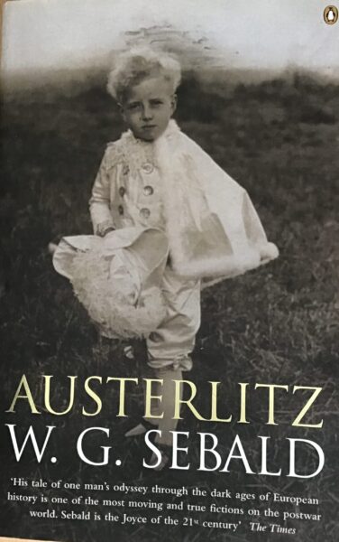 Early photograph. A boy with blond hair wears a white suit with a fur edged cape and holds a tricornered white hat. He looks into the camera with an intent gaze and stands in a militaristic pose.